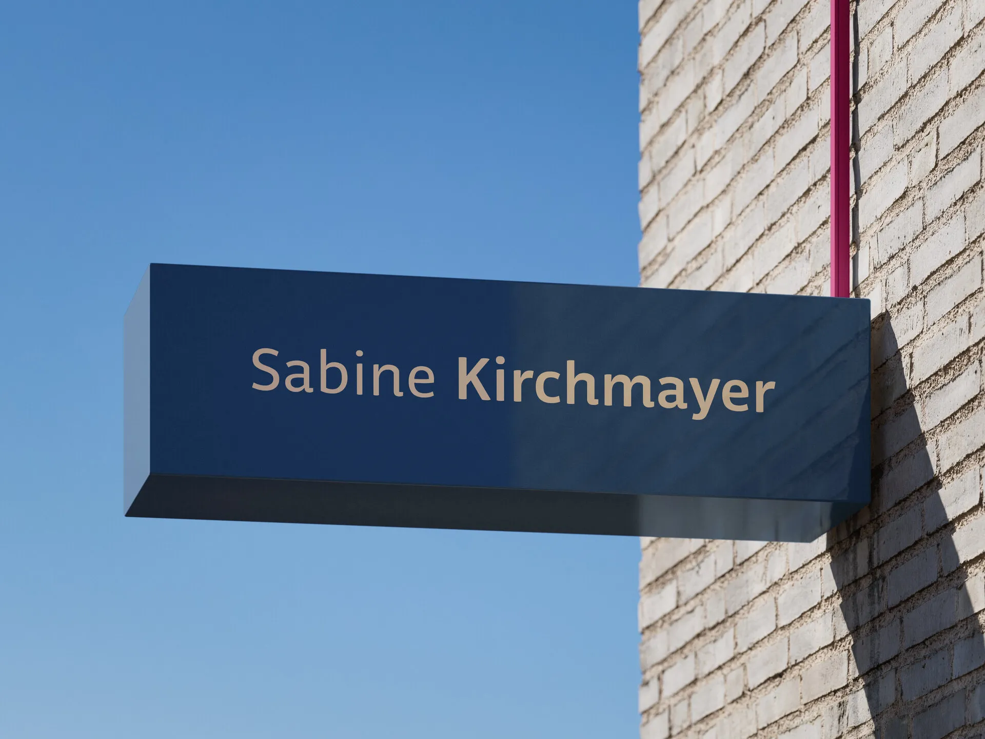 Blauer Leuchtkasten mit dem Schriftzug Sabine Kirchmayer an einer hellen Ziegelfassade