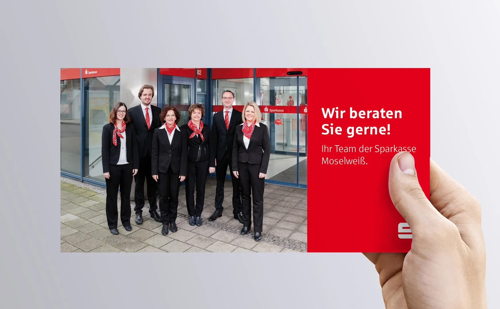 Hand hält Flyertitel Wir beraten Sie gerne mit Teamfoto der Sparkasse Moselweiß