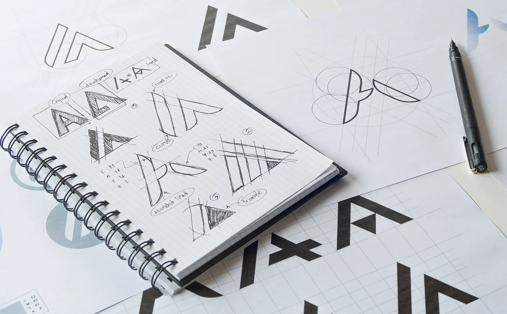 Aufgeschlagenes Notizbuch mit Bleistiftskizzen und Konstruktionslinien für einen neuen Logoentwurf