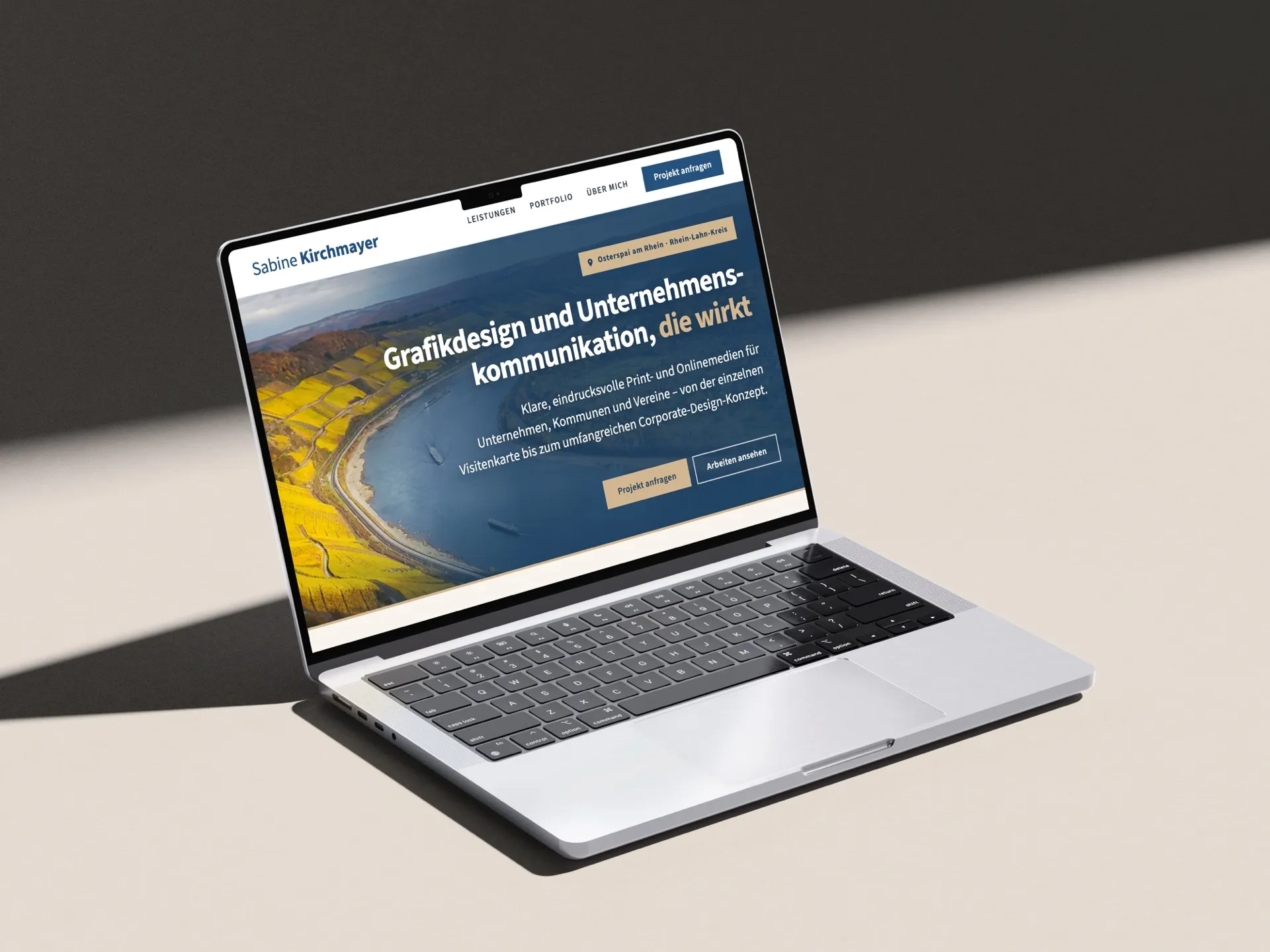Aufgeklappter Laptop auf hellem Tisch, auf dem Bildschirm die Startseite mit Rheinpanorama