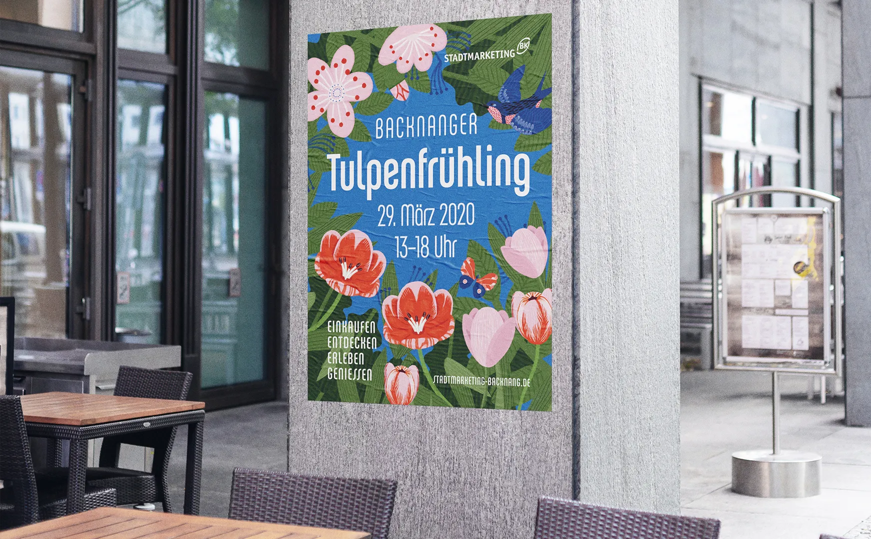 Plakat zum Backnanger Tulpenfrühling an einer Hauswand neben einem Café mit Stühlen