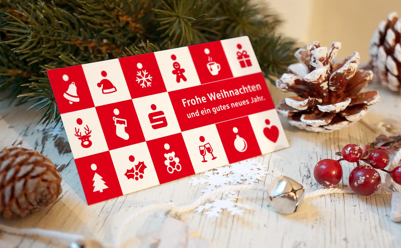 Weihnachtskarte der Sparkasse Koblenz mit rot-weißem Piktogrammraster zwischen Tannenzweigen und Zapfen