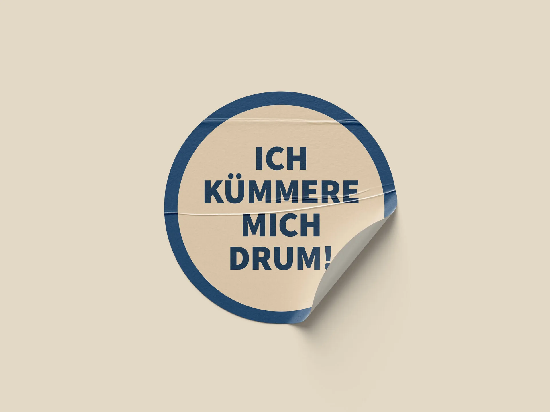 Runder Aufkleber mit dem Satz „Ich kümmere mich drum!“ in Blau auf Champagner, eine Ecke leicht abgelöst